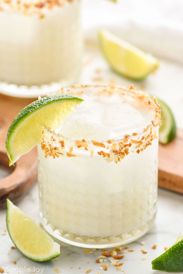 close up of a coconut margarita in a glass rimmed with toasted coconut and garnished with a lime wedge