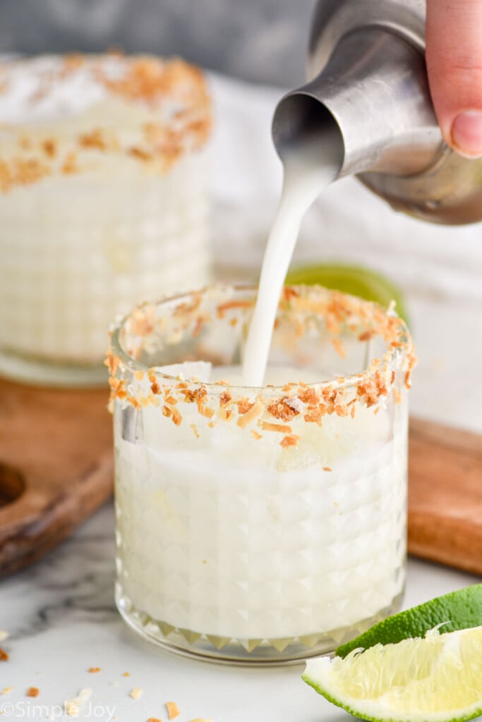 coconut margaritas recipe being poured into a tumbler rimmed with toasted coconut