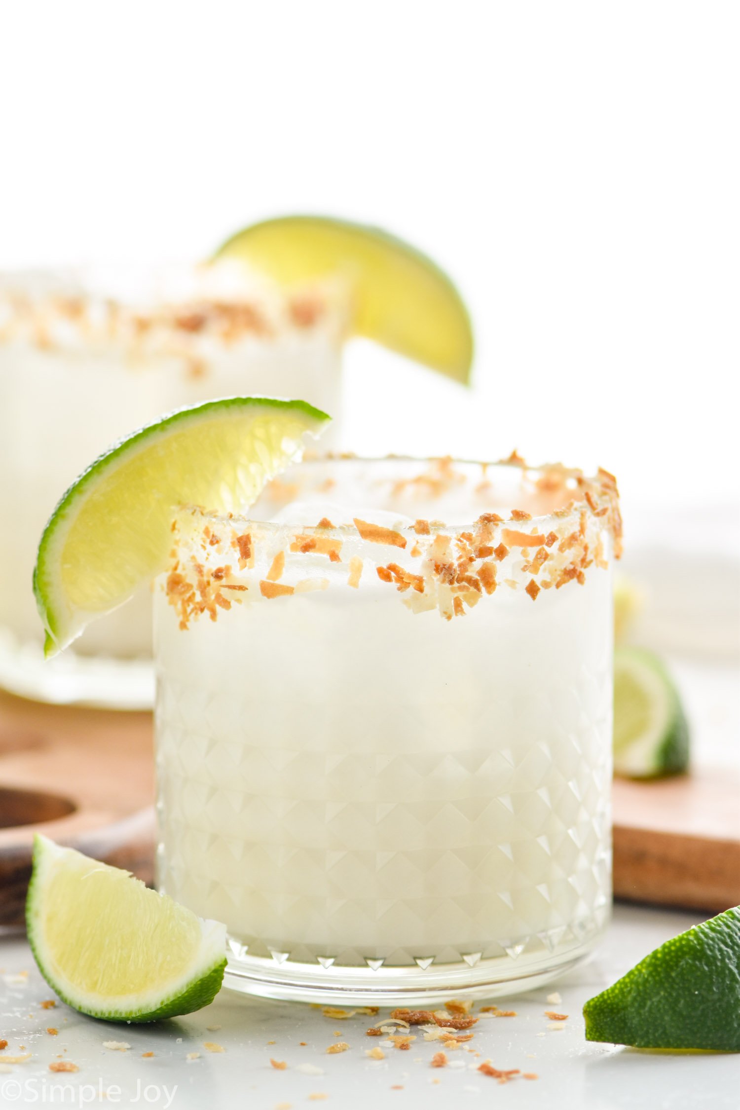 two tumblers filled with coconut margaritas, garnished with toasted coconut and lime wedges
