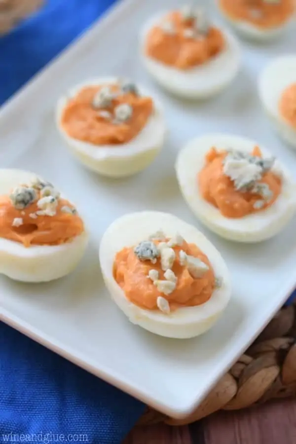 On a white plate, the Buffalo Deviled Eggs are lined up and topped with Blue Cheese crumble. 