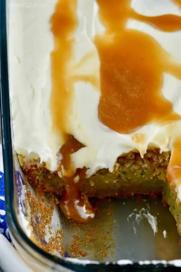 In a glass casserole dish, the Zucchini Poke Cake is topped with some white frosting and drizzled with caramel. 