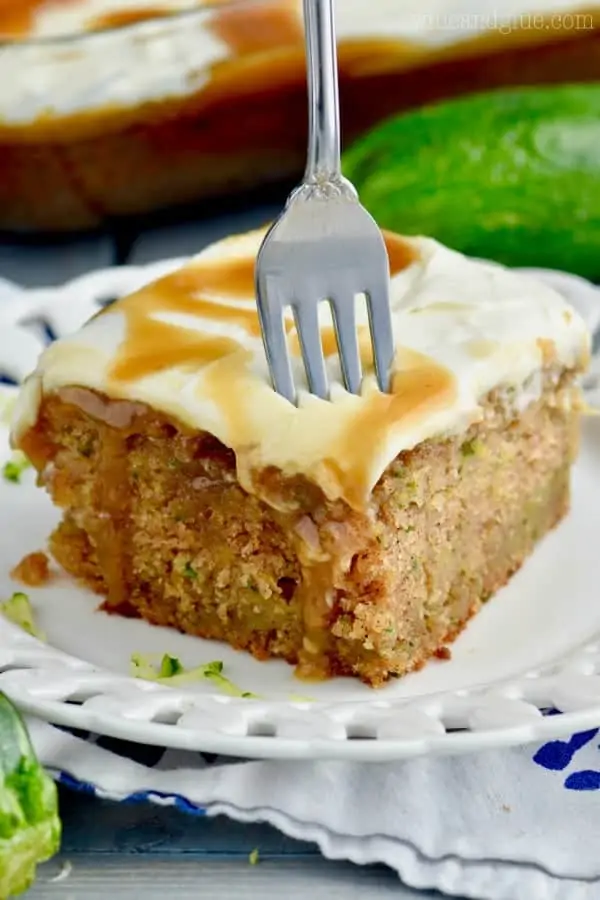 A fork digging into the Caramel Zucchini Poke Cake has a moist interior and drizzled with caramel. 