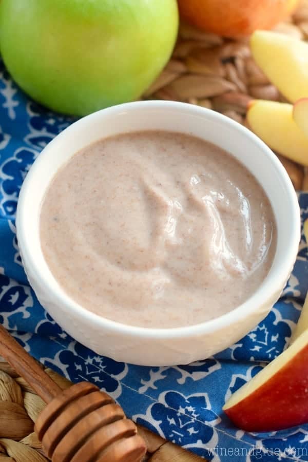 A small serving bowl with a smooth glossy brown dip surrounded by sliced apples