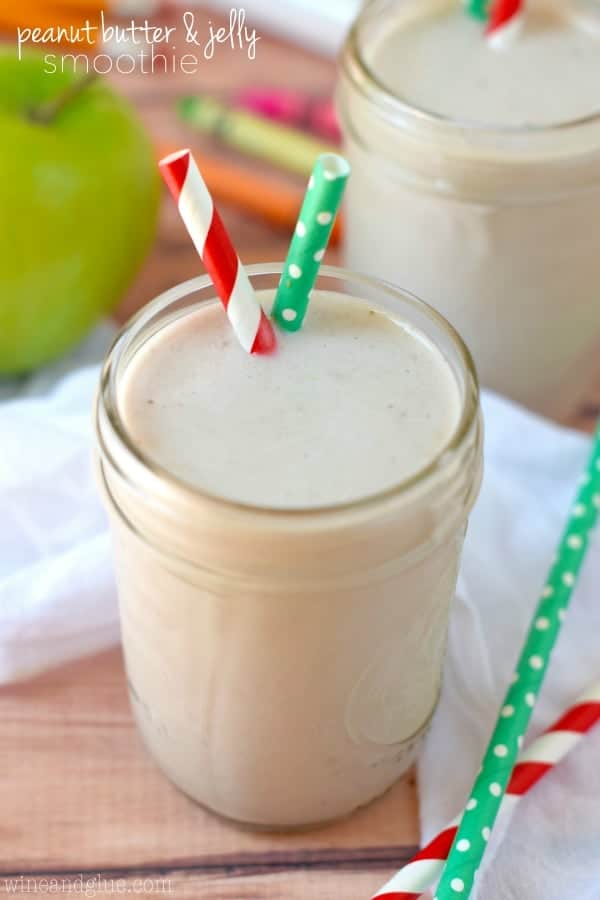 In a mason jar, the Peanut Butter and Jelly Smoothie has an off white color with two paper straws. 
