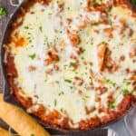 overhead view of a skillet lasagna in a gray skillet on a cooling rack with two breadsticks next to it
