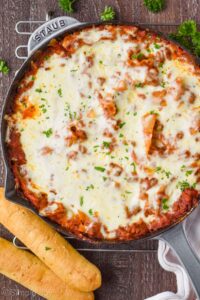 overhead view of a skillet lasagna in a gray skillet on a cooling rack with two breadsticks next to it