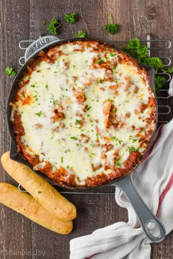 overhead of a gray skillet on a wood surface with skillet lasagna and two breadsticks next to it
