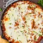 overhead view of a skillet lasagna in a gray skillet on a cooling rack with two breadsticks next to it