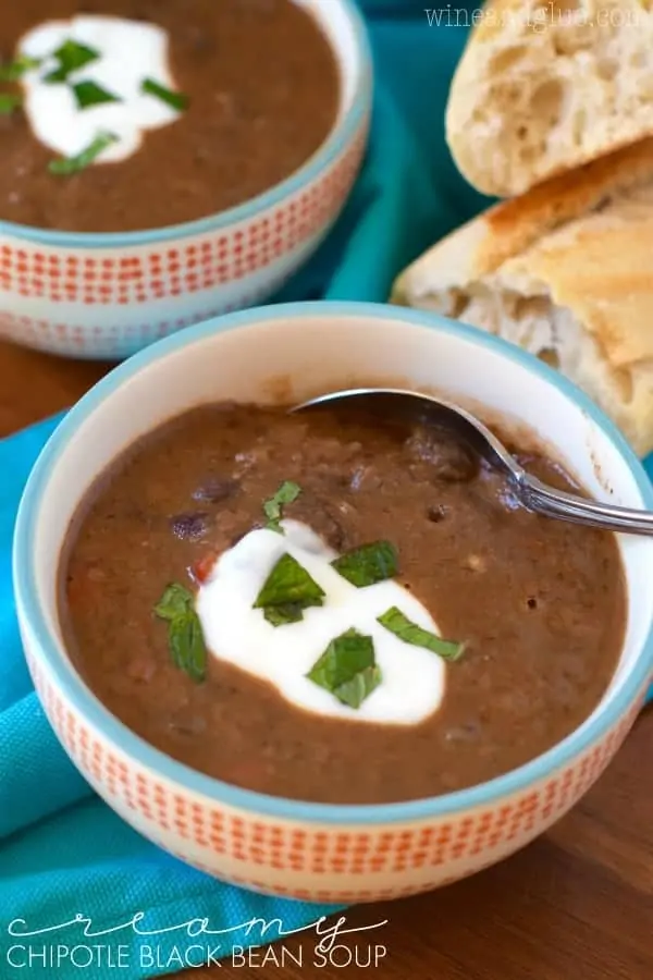 In a colorful bowl, the Creamy Vegan Black Bean Soup has a dollop of sour cream in the middle topped with cilantro. 