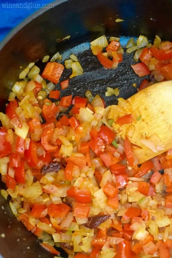 In a cast iron pan, diced white onion, red bell peper, and jalapenos are being sauteed in olive oil. 