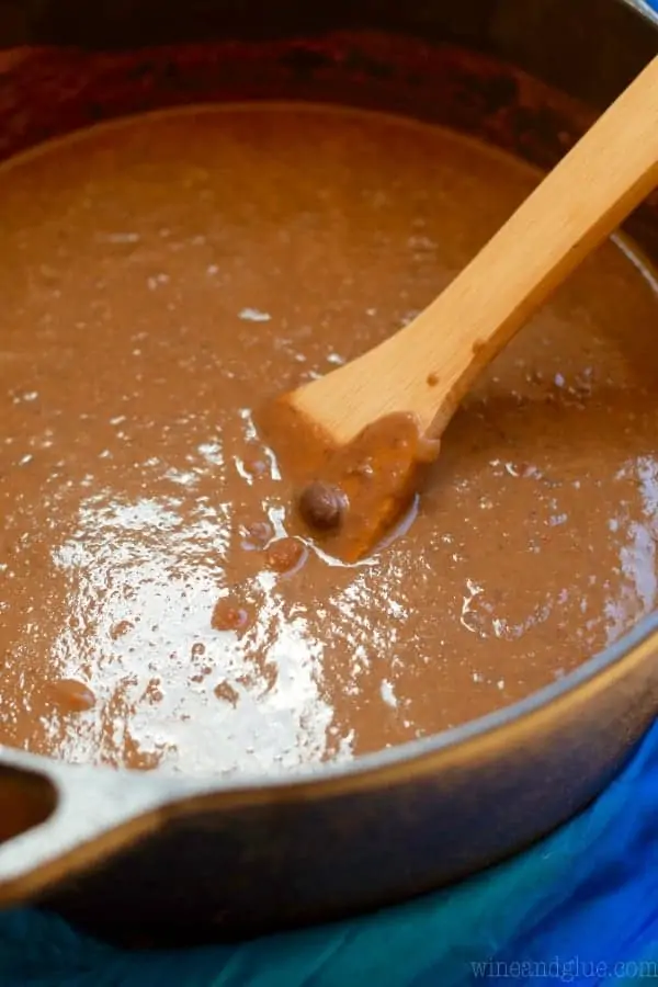 In the cast iron, dish a wooden spatula is stirring the Creamy Vegan Black Bean Soup. 