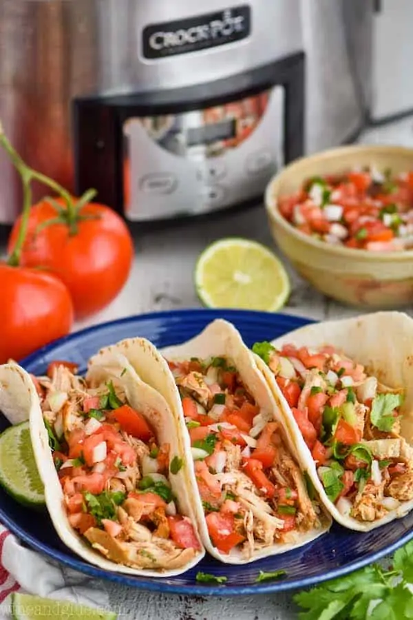 three tacos on a blue plate in front of a crockpot