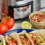 three tacos on a blue plate in front of a crockpot