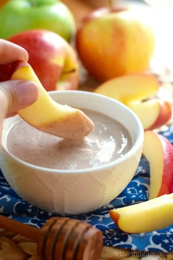 An apple slice being dipped in the brown, glossy, and smooth dip which is in a small serving bowl