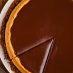 overhead view of a pumpkin cheesecake covered in chocolate ganache with one piece cut into