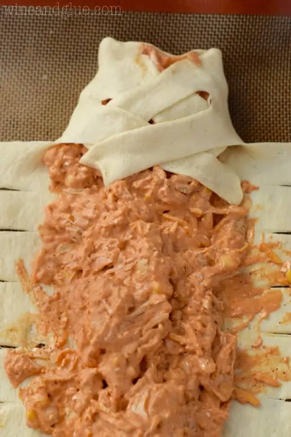 The crescent roll dough is being braided on top of the filling. 