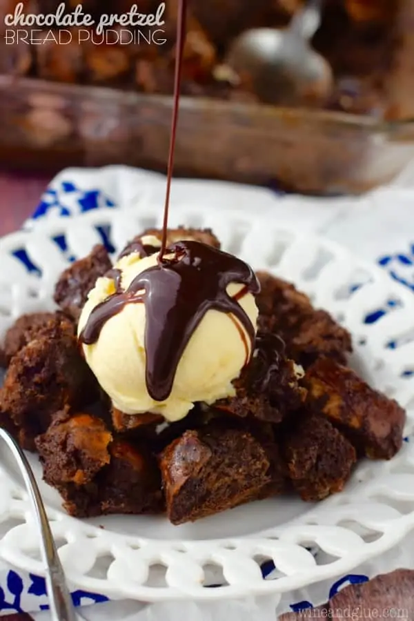 On a white plate, the Chocolate Pretzel Bread Pudding has a scoop of vanilla ice cream with chocolate being drizzled on top. 