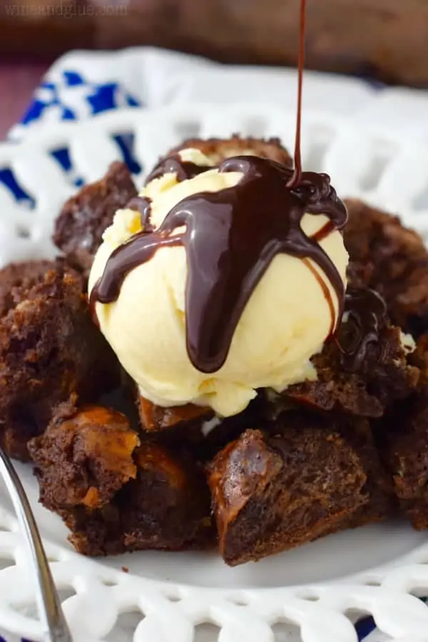 On a white plate, the Chocolate Pretzel Bread Pudding has a scoop of vanilla ice cream with chocolate being drizzled on top. 