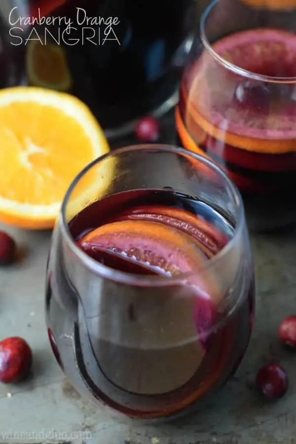 The Cranberry Orange Sangria are in a tumbler wine glass with a dark purple complexion.  