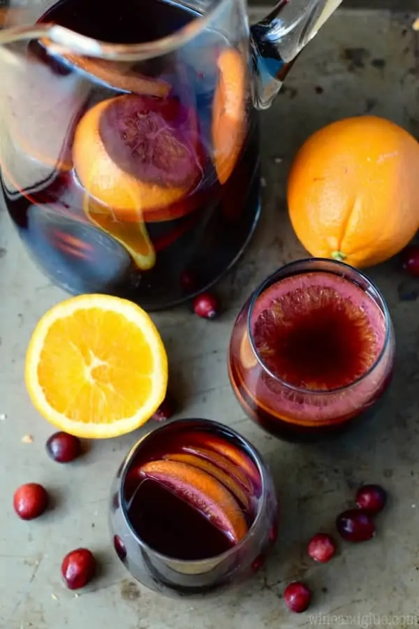 An overhead photo of the Cranberry Orange Sangria in two tumbler glasses and a pitcher with sliced oranges in the shape of a circle. 