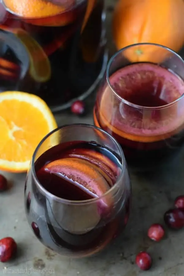 The Cranberry Orange Sangria are in a tumbler wine glass with a dark purple complexion.  