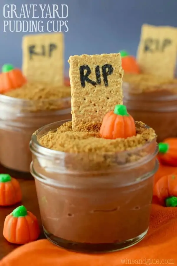 In a small mason jar, the Pumpkin spice Chocolate Pudding is topped with crushed graham cracker, a pumpkin candy, and a stick of a graham cracker with the letter RIP. 