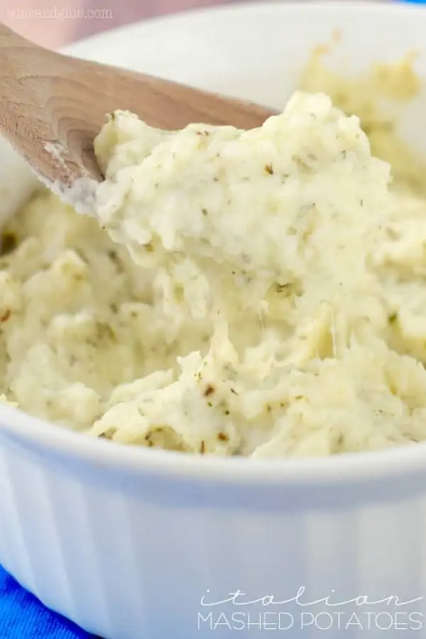 The Italian Mashed Potatoes is in a ceramic white dish with a spoon digging into it. 