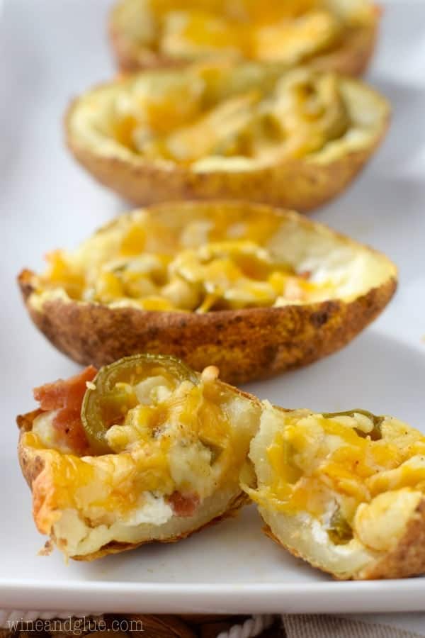 The Jalapeno Popper Potato Skins is cut in half showing the cream cheese filling, jalapenos, bacon, and a sheet of melted cheese. 