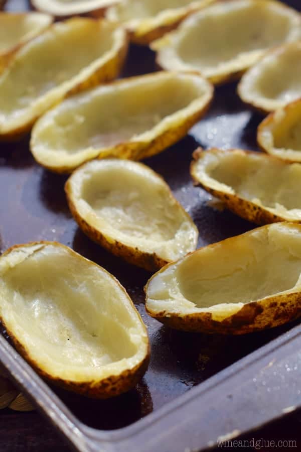 On a baking sheet, potatoes are sliced in half and carved out. 