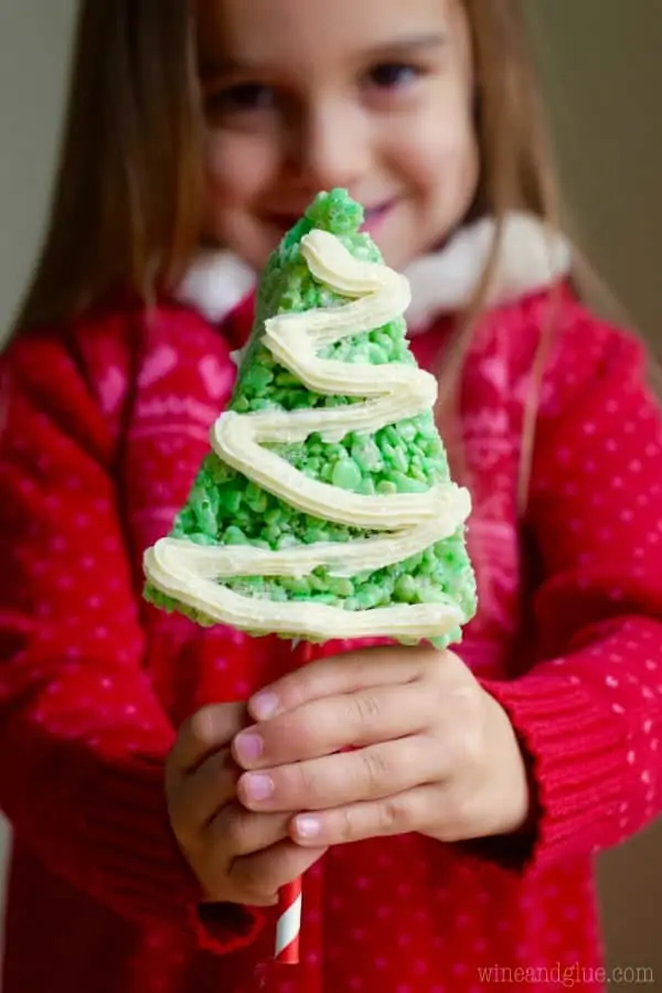 A little girl is holding the Rice Krispie Treat Christmas Tree which is green and triangular with white frosting in a zig zag pattern. 