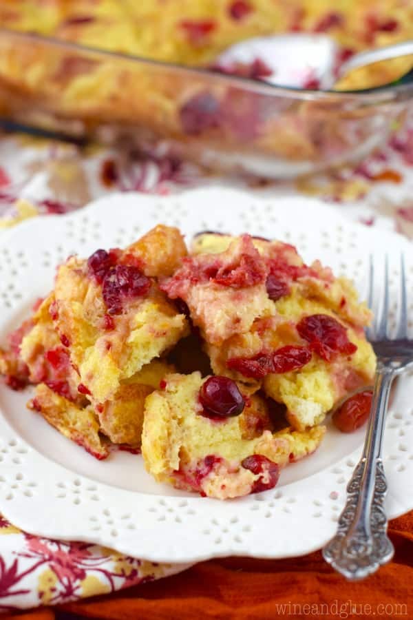On a white plate, the Cranberry Orange Bread Pudding has beautiful golden color with speckles of red from the cranberries. 