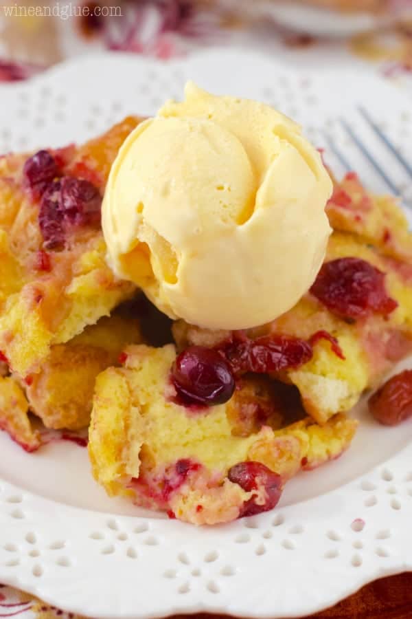 On a white plate, the Cranberry Orange Bread Pudding has a scoop of a vanilla ice cream on top. 