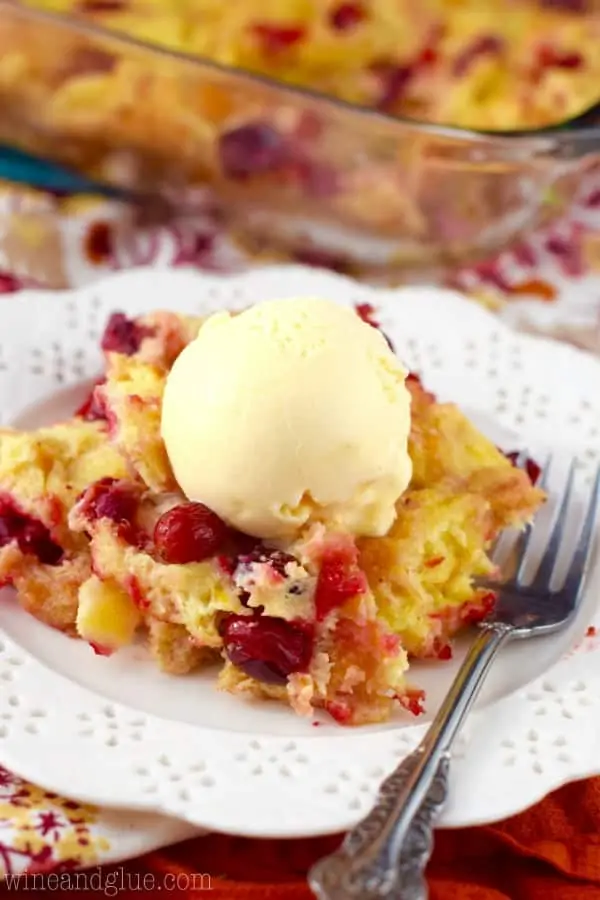 On a white plate, the Cranberry Orange Bread Pudding has a scoop of a vanilla ice cream on top. 