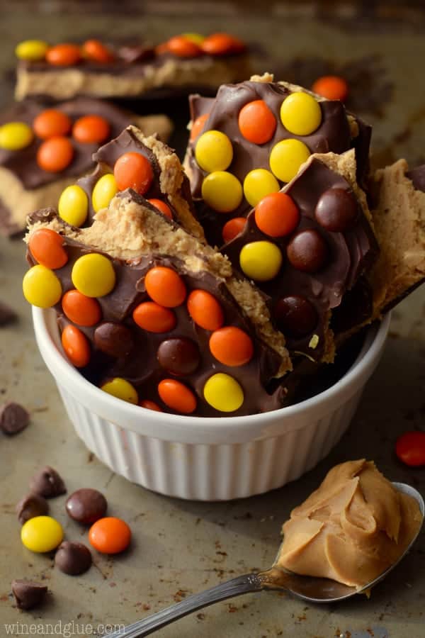 In a ceramic bowl, the Loaded Reese's Peanut Butter Cup Bark are cut in little shards and topped with chocolate and Reese's Pieces.