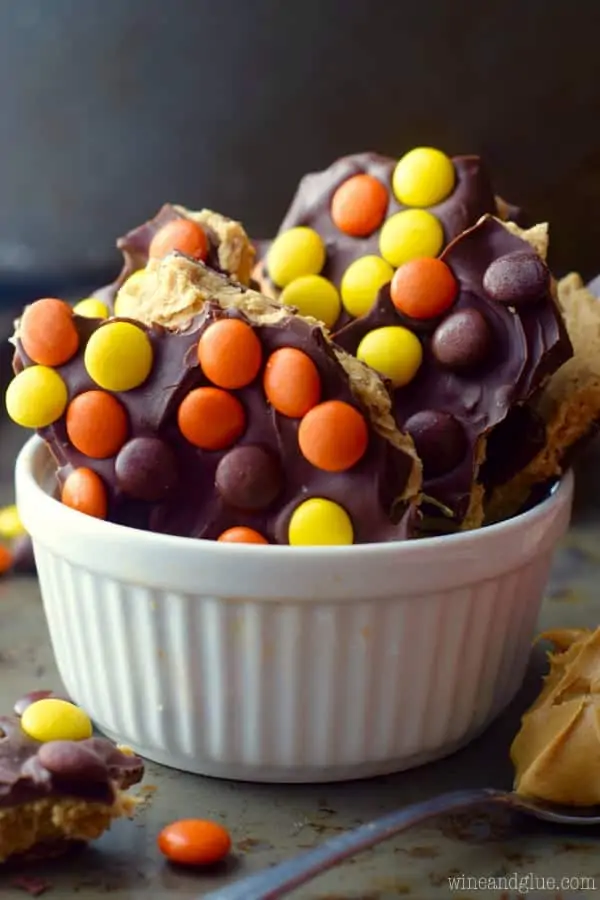 In a ceramic bowl, the Loaded Reese's Peanut Butter Cup Bark are cut in little shards and topped with chocolate and Reese's Pieces.