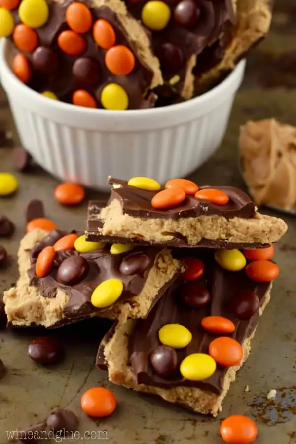 A stack of the Loaded Reese's Peanut Butter Cup Bark has a light brown layer topped with chocolate and Reese's Pieces. 