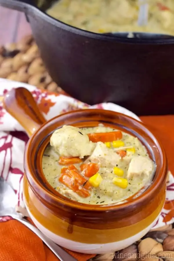 In a brown ceramic bowl, the Turkey Dumpling Soup has chunks of turkey, balls of dumpling, slices of carrots, and corn in a creamy broth. 