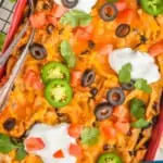 pinterest graphic of overhead view of a chicken taco casserole in a red baking dish garnished with sour cream, jalapeños, olives, and cilantro