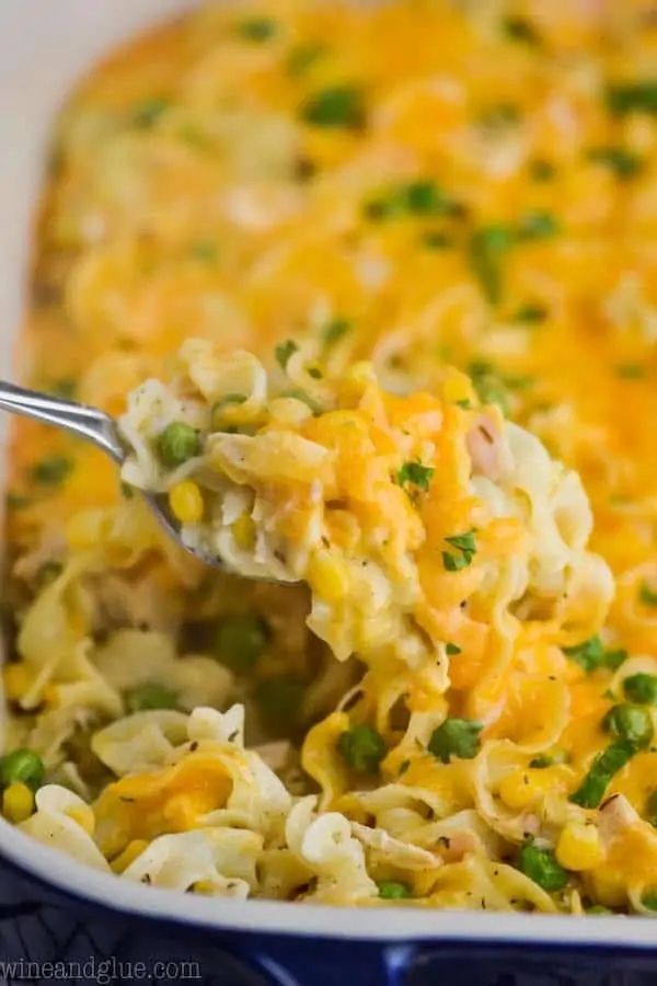 a spoon dishing into a casserole dish lifting up cheesy noodles that have been garnished in fresh parsley
