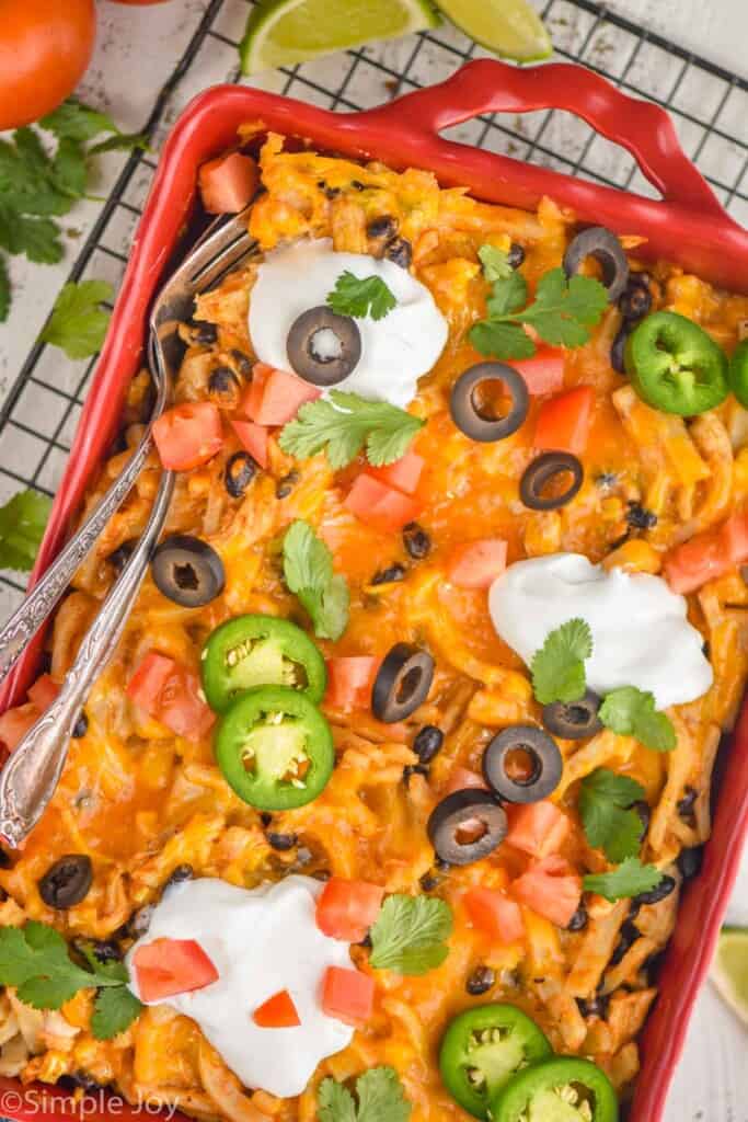 overhead view of a chicken taco casserole in a red baking dish garnished with sour cream, jalapeños, olives, and cilantro