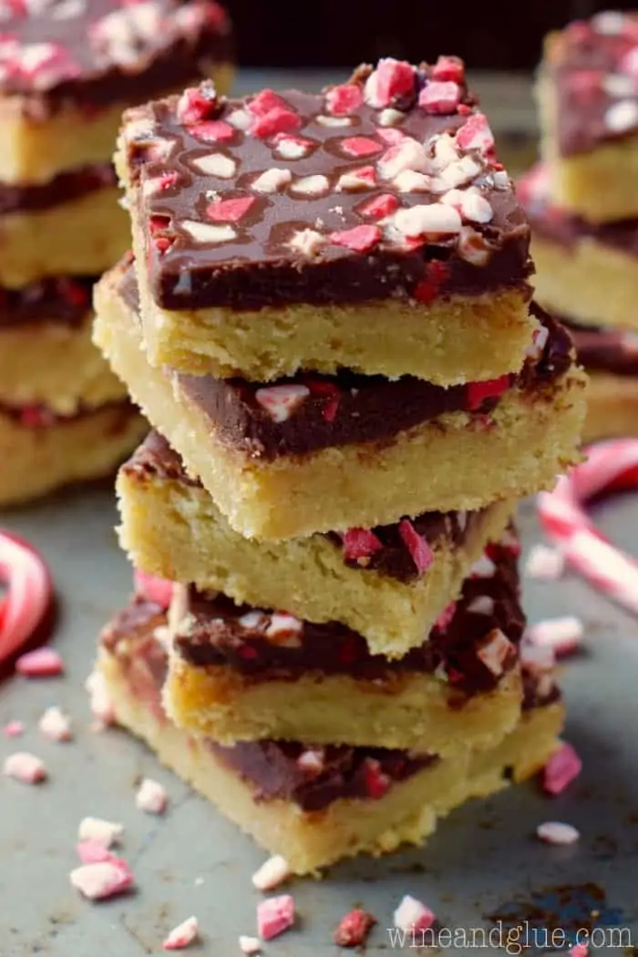 The the Chocolate Peppermint Sugar Cookie Bars is stalked high showing the distinct layers of the sugar cookie and chocolate and topped with crushed peppermint