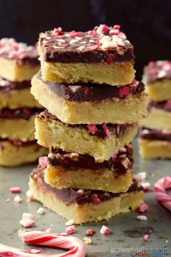The the Chocolate Peppermint Sugar Cookie Bars is stalked high showing the distinct layers of the sugar cookie and chocolate and topped with crushed peppermint