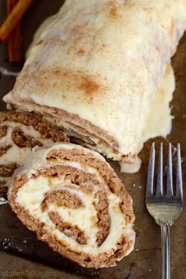 An overhead photo of two slices of the Cinnamon Cake Roll next to the cake roll showing the buttercream filling and topped with a glaze. 