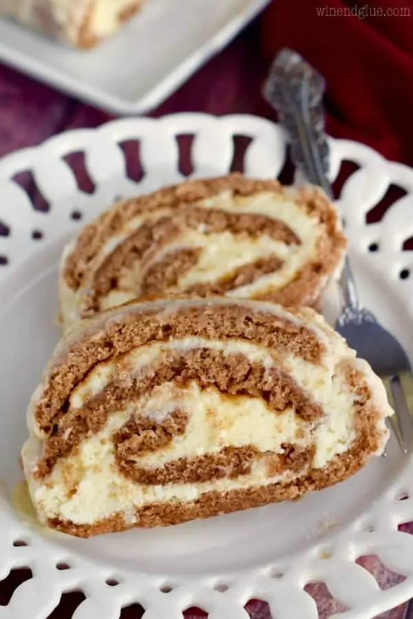 On a white plate, two slices of the Cinnamon Cake Roll is rolled up with a buttercream frosting in a spiral shape. 