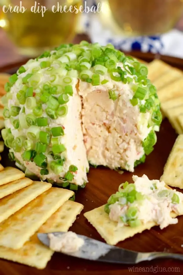 Surrounded by crackers, the Crab Cheese Ball has a large slice cut out and topped with chives. 