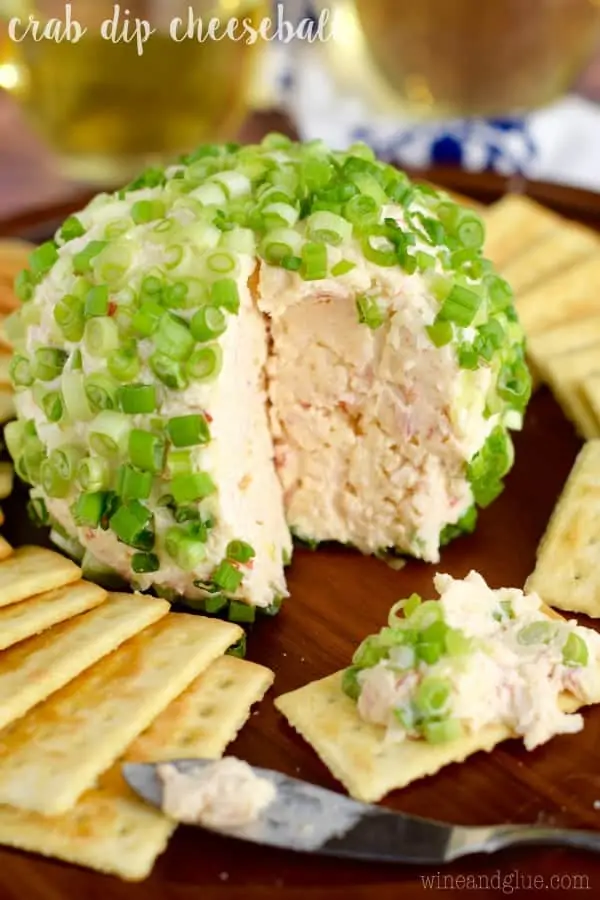 The Crab Dip Cheeseball has a a big slice showing the light pink inside and topped with cut scallions. 