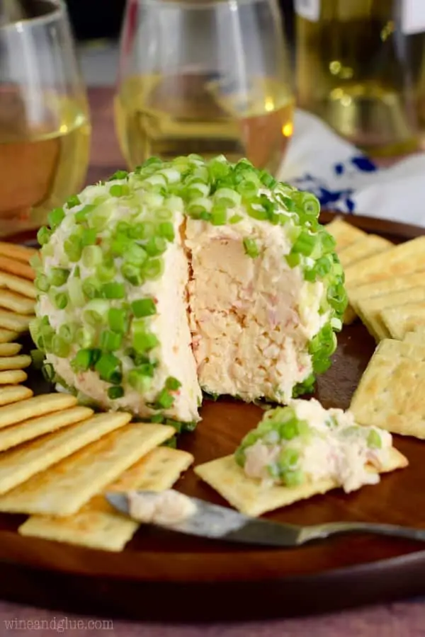 The Crab Dip Cheeseball has a a big slice showing the light pink inside and topped with cut scallions. 