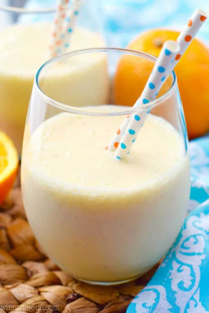 In a glass, the Orange Colada Smoothie has a pastel yellow color with two paper straws. 