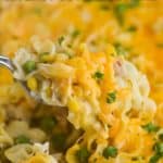 a spoon dishing into a casserole dish lifting up cheesy noodles that have been garnished in fresh parsley
