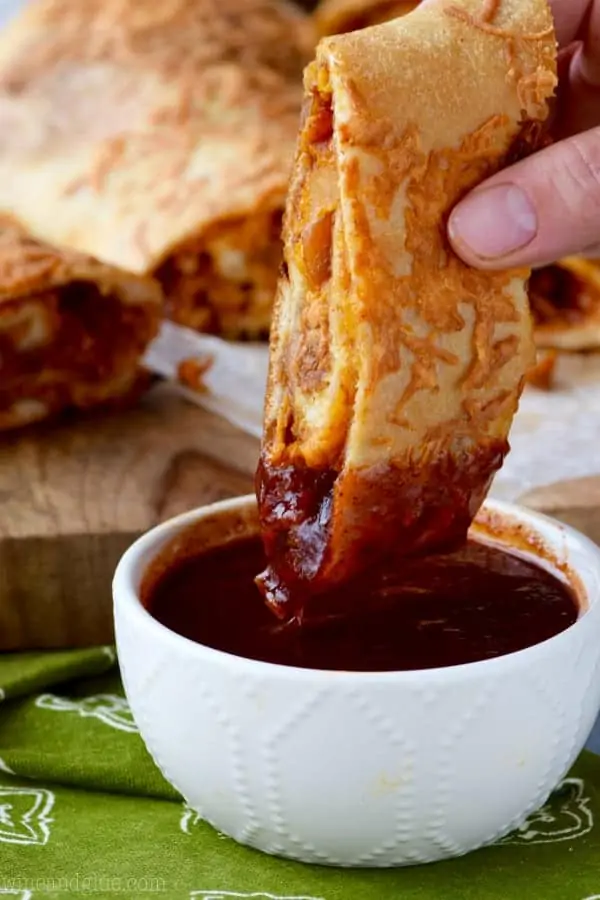 A slice of BBQ Chicken Pizza Roll is being dipped into BBQ sauce. 